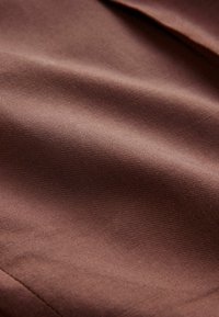 Brown woven fabric with a smooth texture, showcasing a subtle sheen and slight ridges, forming gentle folds and creases.