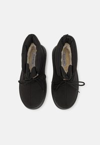 Paire de chaussures d'hiver noires rembourrées avec doublure en fourrure et lacets noirs, vues de dessus sur fond blanc.