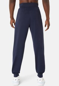 Marine joggers gemaakt van zachte, rekbare stof met een taps toelopende pasvorm, elastische tailleband en subtiele stikdetails. Gepaard met witte sportschoenen.