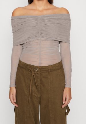 Olkapäät paljastava, röyhelöity taupenvärinen pitkähihaispaita yhdistettynä korkeavyötäröisiin, ruskeisiin cargo-housuihin, joissa on kiristysnyöri ja suuret etutaskut.