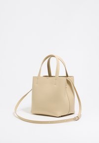 Beige leather tote bag with a textured finish, two top handles, and an adjustable shoulder strap. Compact and square-shaped design.