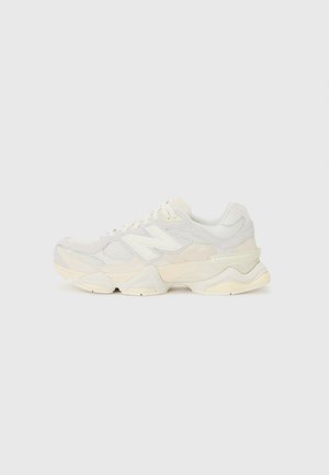Biało-beżowy sneaker New Balance z panelami z siateczki i skóry, grubą podeszwą i sznurowaniem, pokazany z boku na jednolitym tle.