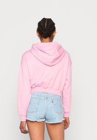 Oříznutá růžová mikina s kapucí, žebrovanými manžetami a lemem, kombinovaná se světle modrými džínovými šortkami s roztřepeným okrajem a jemným vzorem.