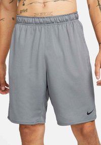 Sivé športové šortky s elastickým pásom a bočnými vreckami. Majú hladkú textúru a malé čierne logo Nike na dolnej ľavej strane.