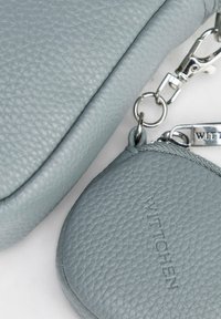 Pochette e portafoglio in pelle grigia con superficie texturizzata, hardware argentato e dettagli con logo impresso. Forma compatta e arrotondata con chiusura a zip.