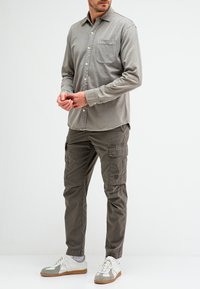Lichtgrijs lange mouwen overhemd met een borstzak, gecombineerd met donkergroene cargobroeken met zijzakken en een relaxte pasvorm, gedragen met sneakers.