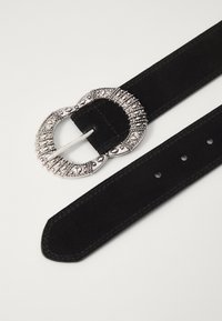 Svart semsket belte med en sirkulær, metallisk sølvspenne med intrikate detaljer. Glatt tekstur med flere justeringshull.