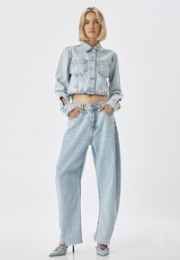 Chaqueta de mezclilla cortada en azul claro con dos bolsillos en el pecho, combinada con jeans de tiro alto y pierna ancha con dobladillos deshilachados.