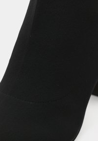 Stivaletto nero realizzato in tessuto testurizzato; presenta un design aderente con punta arrotondata e dettagli di cuciture lisce.