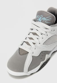 Sapatilha atlética cinza e branca com parte superior em rede, textura de camurça suave, cadarços planos e colarinho acolchoado com detalhe em azul no logotipo.