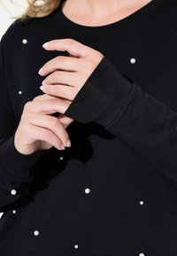 Top nero a maniche lunghe con scollatura rotonda, caratterizzato da gruppi di piccoli perle bianche e polsini aderenti. Il tessuto sembra morbido con una leggera elasticità.