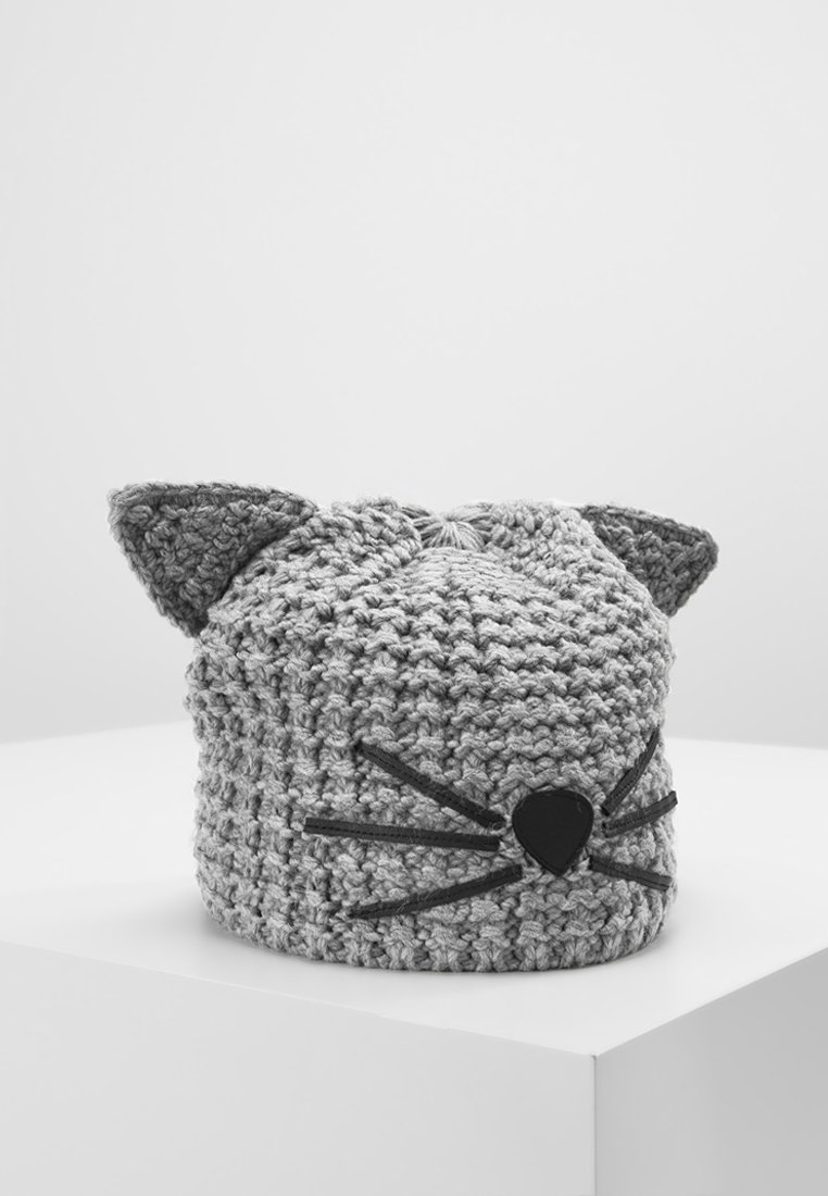 Bonnet tricoté gris avec des oreilles de chat, un nez noir en forme de cœur et des moustaches, exposé sur un socle blanc sur un fond uni.