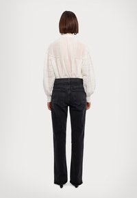 Hvid, langærmet, struktureret bluse med puffede ærmer, parret med højtsiddende, sorte, lige ben jeans. Bagfra, ingen synlige detaljer.