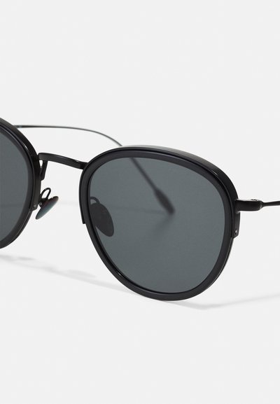 Round black sunglasses ar tumšiem lēcu tonējumiem. Plāna metāla rāmī ar elegantu dizainu un regulējamiem deguna paliktņiem ērtībai.