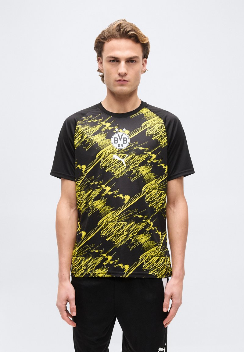 Νεαρός άνδρας που φοράει μαύρη και κίτρινη φανέλα ποδοσφαίρου της Borussia Dortmund BVB 09 με λογότυπα Puma, στέκεται μπροστά σε ένα απλό λευκό φόντο.