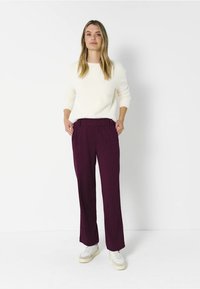 Un pull blanc et un pantalon à rayures violettes foncées, coupe droite, avec des poches latérales, associés à des baskets blanches sur un fond uni.