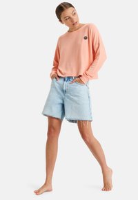 Rosa Langarm-Sweatshirt mit einem kleinen Sonnenmotiv, kombiniert mit hellblauen Jeansshorts mit fransigem Saum und lockerer Passform.