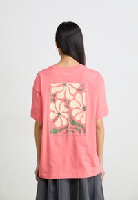 Roze katoenen T-shirt met een oversized pasvorm. Voorzien van een bloemrijke grafiek in crème en groen, gecentreerd op de achterkant. Casual ontwerp met korte mouwen.