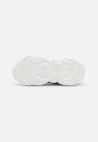 Weiße Sneaker-Sohle mit einem Bärenkopf-Design, strukturiertem Oberflächen und geprägtem Text, der "DAS IST KEIN MOSCHINO SPIELZEUG" lautet.