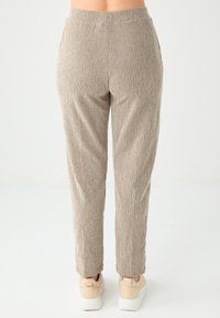 Jasnobrązowe spodnie teksturowane z elastycznym pasem i zwężanymi nogawkami, w połączeniu z beżowymi trampkami. Widok z tyłu pokazuje dwie boczne kieszenie.