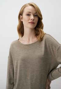 Beige Langarmoberteil aus weichem, strukturiertem Stoff. Verfügt über einen lockeren Schnitt und einen leicht weit geschnittenen Halsausschnitt. Gleichmäßige, glatte Farbgebung.