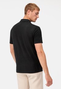 Schwarzes Poloshirt mit kurzen Ärmeln, weichem Material und klassischem Kragen, mit geradem Saum und lockerer Passform.