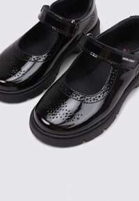 Zapatos Mary Jane de charol negro con detalles perforados, suelas de goma gruesa y correas ajustables de gancho y bucle.