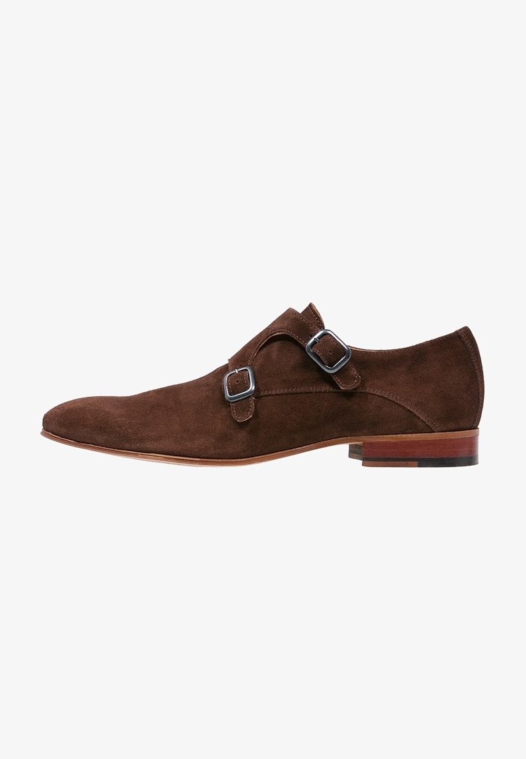 Scarpa in suede marrone dal design elegante, con accenti a doppia fibbia e punta affusolata. La suola è in legno con una finitura liscia.
