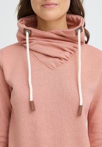 Sudadera rosa con diseño de cuello vuelto, con textura fruncida, cordones blancos y detalles de cuero marrón.