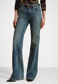 Uformede blå denimjeans med en falmet vask, høy midje og fem-lommers design. Har kontrasterende sømmer og et svart belte med en sølvspenne.