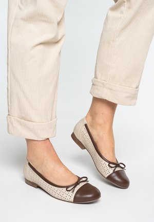 Noge u bež plisiranim hlačama uzorkom u prugice, sa preklopljenim rubovima, i bež balerinkama s tamnobraon vrhovima i malim ukrasnim mašnama.