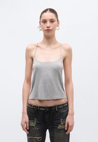 Hall hallist puuvillast kamisol õhukeste spagettrihmadega, millel on lõdvestunud istuvus ja ümar kaelus, sobitatud kulunud tume teksapükstega, millel on naelad.