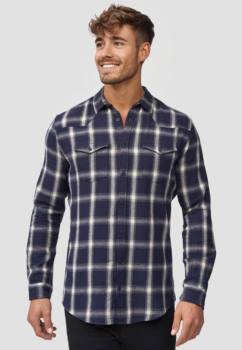 Navy plaid flannel shirt with white lines, button-up design, two chest pockets, long sleeves, and curved hem detailing.