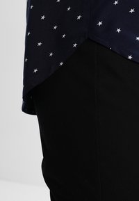 Mörkblå skjorta med vitt stjärnmönster, som har en något rundad fåll, tillsammans med svarta byxor i tyg.