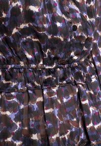 Bluse mit einem mehrfarbigen abstrakten Muster in lila, schwarz und braun. Rüschendetail an der Taille und Knopfakzente.
