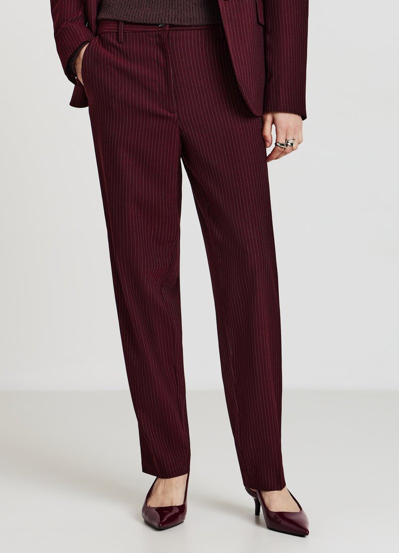 Pantalon bordeaux à fines rayures, coupe ajustée, confectionné dans un tissu texturé. Porté avec un haut uni marron foncé et des talons assortis bordeaux.