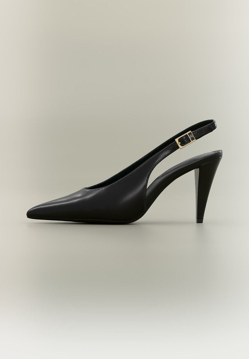 Μαύρο δερμάτινο γόβα με μυτερή ανοιχτή φτέρνα, χρυσή αγκράφα και λεπτή τακούνι σε ουδέτερο φόντο.