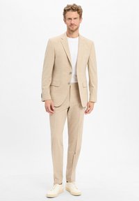 Beżowa marynarka i spodnie z delikatnym wzorem, w połączeniu z białym t-shirtem i kremowymi trampkami. Dopasowany krój, zapinany na dwa guziki, z bocznymi kieszeniami.