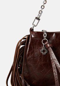 Bruine leren handtas met een glanzende afwerking, voorzien van franjes, een zilverkleurige kettingband en een decoratieve metalen hanger.
