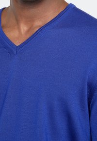 Blauer V-Ausschnitt-Pullover mit gerippter Textur, aus einem weichen Strickstoff gefertigt. Der Ausschnitt hat einen schmalen, sauberen Rand.