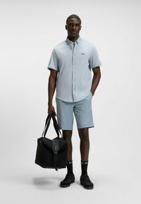 Light blue short-sleeved button-up shirt with a pocket, paired with light blue shorts. Black bag with a zipper, black shoes, and socks with logo.