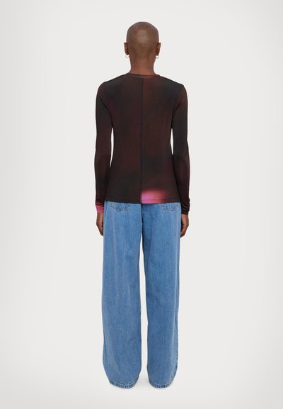 Maglietta a maniche lunghe, aderente, nera con una sfumatura da rosa scuro a rosa chiaro in vita; abbinata a jeans in denim azzurro a gamba larga.