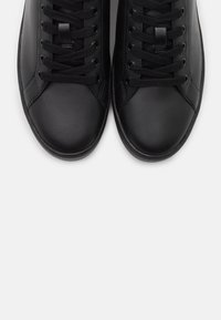 Baskets en cuir noir avec une texture lisse, un bout arrondi, des lacets plats, un minimum de coutures et un design profilé bas.