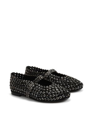 Czarne płaskie buty ozdobione okrągłymi srebrnymi ćwiekami, z falistymi krawędziami i paskiem zapinanym na krzyż. Teksturowana powierzchnia, niska podeszwa.