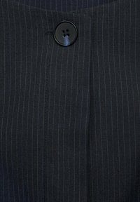 Black fabric with subtle vertical pinstripes in blue. Features a prominent black button and stitching detail along the edges.