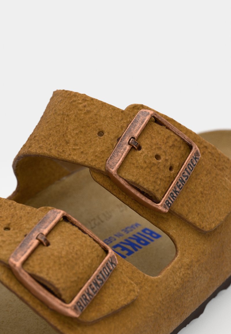 Sandale en daim marron avec des boucles réglables en cuivre à double réglage, un semelle anatomique et un marquage bleu sur la semelle intérieure.