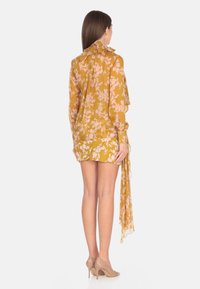 Vestito floreale giallo con maniche lunghe, tessuto trasparente, colletto arricciato e design a portafoglio, caratterizzato da fiori rosa e un dettaglio posteriore fluente.