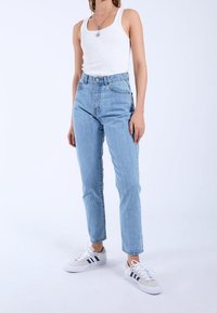 Ljusblå högmidjade jeans med rak benklippning, med en klassisk femficksdesign och subtila blekningar. Tillsammans med en vit linne och sneakers.