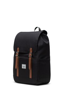 Black fabric backpack with a fold-over flap, brown leather straps, and silver hardware. Features a front pocket and a logo patch.