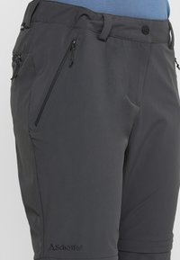 Pantalones cortos de senderismo grises, hechos de una tela suave y ligera, con bolsillos con cremallera y un detalle de logo en el dobladillo inferior izquierdo.